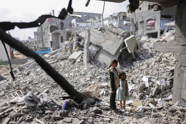 طفلتان فلسطينيتان تقفان وسط أنقاض مبان مدمرة جراء الغارات الإسرائيلية في قطاع غزة (أ.ف.ب) 
