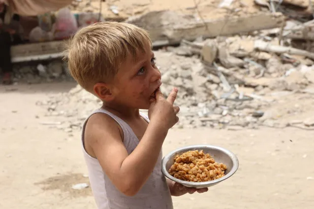 طفل يأكل من صحن طعام حصل عليه من «تكيَّة خيرية» بمدينة غزة اليوم (أ.ف.ب)