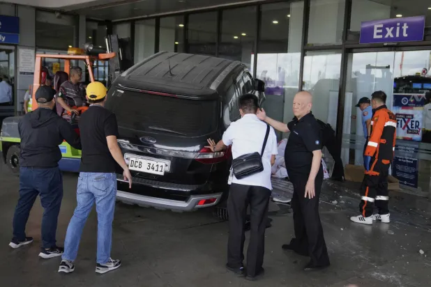 مسؤولون بمطار مانيلا يساعدون أفراد الطوارئ بعدما ارتطمت سيارة بمدخل صالة المغادرة (أ.ب)