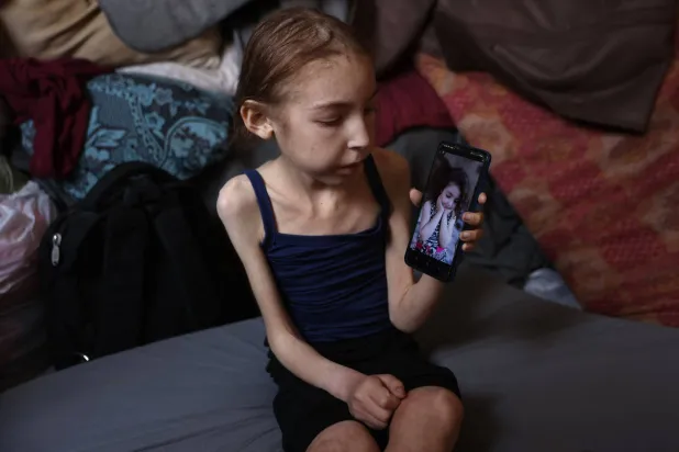 الطفلة الفلسطينية رهف عياد (12 عاماً) التي تعاني سوء تغذية تجلس يوم الأحد في مدرسة بحي الرمال وسط مدينة غزة وتعرض صورة قديمة لها (أ.ف.ب)