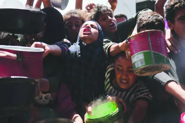 Filistinliler dün Gazze'nin güneyindeki Han Yunus'taki bir yardım mutfağından yiyecek almakta zorlanıyor (AP)