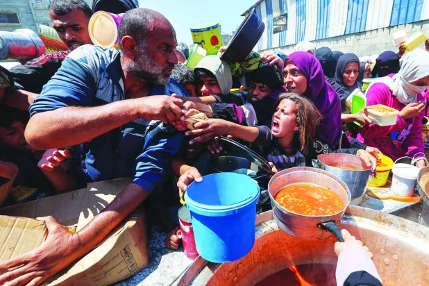 تدافع للحصول على معونة غذائية من مطبخ خيري في مخيم النصيرات وسط قطاع غزة أمس (أ.ف.ب)