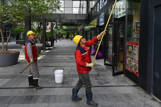 عمال ينظفون واجهة مطعم في بكين (أ.ف.ب)