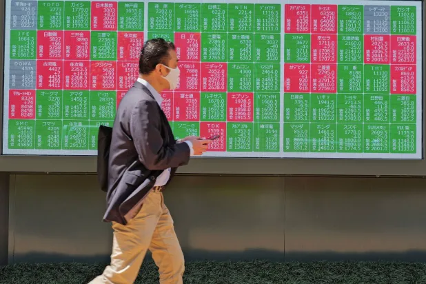 شخص يسير أمام لوحة إلكترونية تعرض مؤشر «نيكي» الياباني في طوكيو (أ.ب)