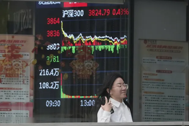 سيدة تمر أمام شاشة تعرض حركة الأسهم في وسط العاصمة الصينية بكين (أ.ب)