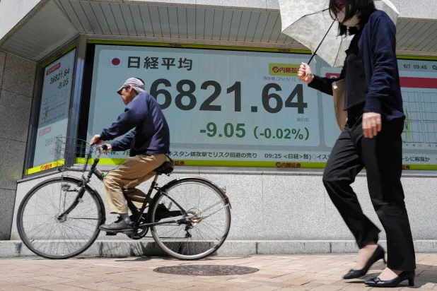 يابانيون يمرون أمام شاشة تعرض حركة الأسهم وسط العاصمة طوكيو (أ.ب)