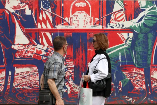 إيرانيان يمران أمام جدارية معادية للولايات المتحدة على حائط سفارتها السابقة في طهران (إ.ب.أ)