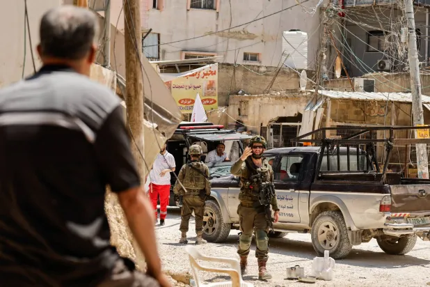 جندي إسرائيلي يلوح بيده بينما يستعد فلسطينيون لإخلاء منازلهم يوم الأربعاء في مخيم نور شمس بالضفة الغربية بعد قرار إسرائيل بهدمها (رويترز)