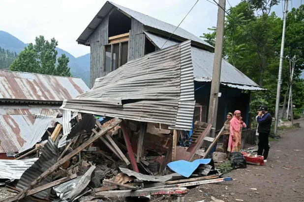 سكان يقفون خارج منزلهم الذي دمره القصف الباكستاني في أثناء استعدادهم للإخلاء في قرية على بعد نحو 100 كيلومتر من سريناغار في 9 مايو (أ.ف.ب)