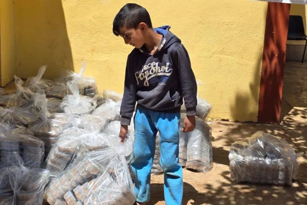 طفل نازح من ريف القصير السورية يتلقى مساعدات غذائية عراقية في شرق لبنان (الشرق الأوسط)