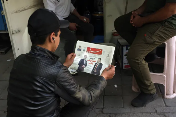 رجل إيراني يقرأ نسخة من صحيفة «شرق» الإيرانية بعنوان «أمل في مفاوضات حقيقية» (إ.ب.أ)