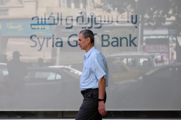 سوري يعبر بنك سوريا والخليج في دمشق وقد ارتفعت قيمة الليرة السورية إلى نحو 8000 للدولار بعد إعلان الرئيس الأميركي دونالد ترمب رفع العقوبات عن سوريا (إ.ب.أ) 