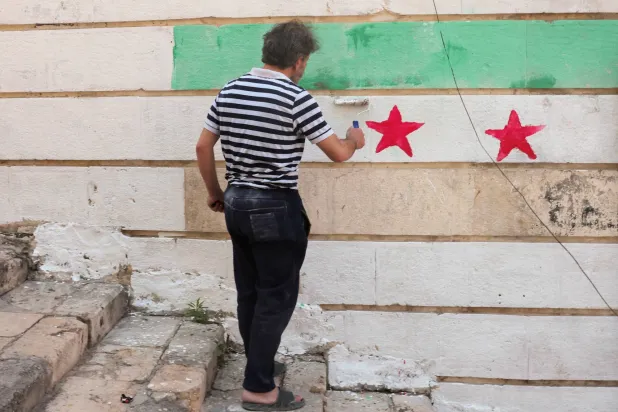 رجل يرسم علم سوريا على جدار (رويترز)