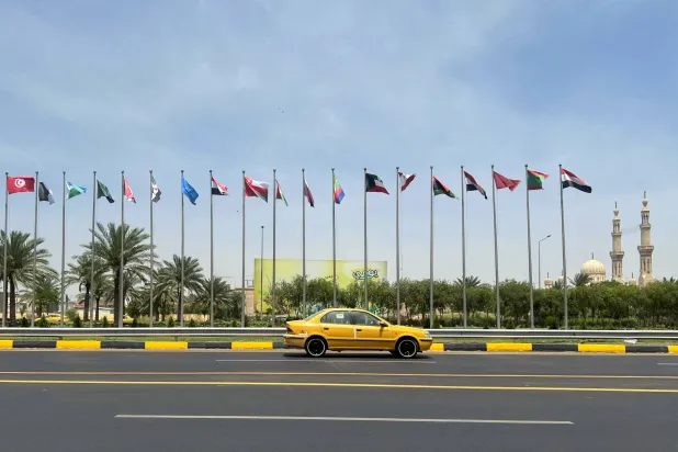 سيارة أجرة تمر أمام أعلام دول أعضاء بجامعة الدول العربية على طول شارع وسط بغداد (رويترز)