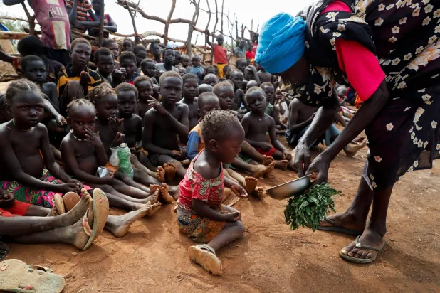 سيدة نازحة تقدم طعاماً لأطفال أيتام في معسكر جنوب كردفان بالسودان (رويترز)