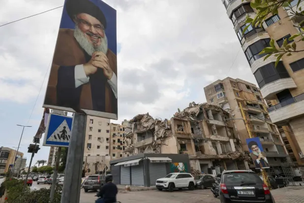 People drive on a street past portraits of slain Lebanese Hezbollah leader Hassan Nasrallah and buildings damaged in Israeli strikes in the recent war, amid the first round of municipal elections, in the Ghobeiry neighborhood of Beirut's southern suburb on May 4, 2025. (Photo by ANWAR AMRO / AFP)