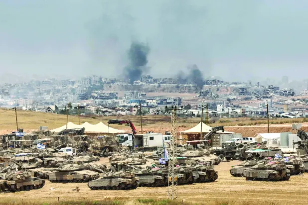 İsrail'in dünkü bombardımanında yıkılan binaların üzerinden dumanlar yükselirken, Gazze Şeridi sınırındaki İsrail araçları (AFP)