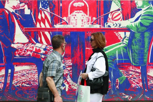 إيرانيان يمران أمام جدارية معادية للولايات المتحدة على حائط سفارتها السابقة في طهران (إ.ب.أ)