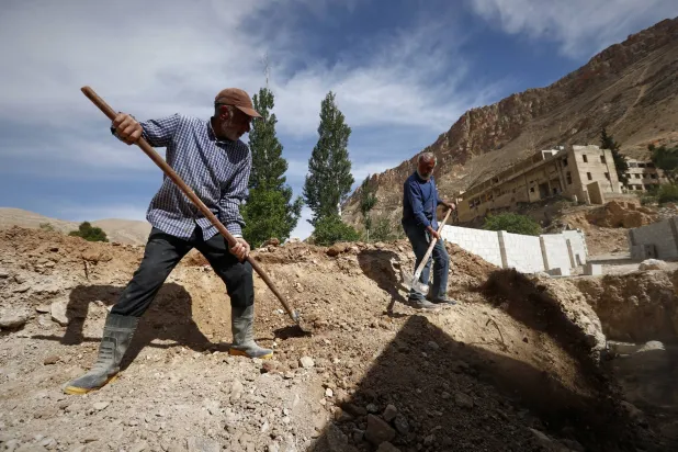 سكان يعملون على إعادة بناء ممتلكاتهم المتضررة خلال الحرب في عين الفيجة بوادي بردى بسوريا (أ.ب)