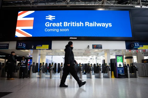 أشخاص يمرون أمام لافتة «سكك حديد بريطانيا العظمة قادمة قريبا» في محطة قطار بوسط لندن (د.ب.أ)