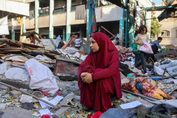 Dün İsrail saldırısı sonucu Gazze'de yerlerinden edilen insanların barındığı bir okulun enkazı arasında oturan Filistinli bir kadın (AFP)