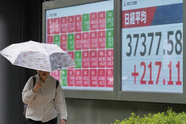 سيدة تمر أمام لوحة إلكترونية تعرض حركة الأسهم في السوق اليابانية بوسط العاصمة طوكيو (أ.ب)