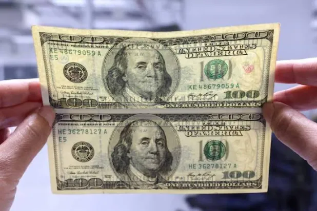 موظف بنك في بانكوك يقارن بين ورقة دولار مزيفة وأخرى أصلية (أرشيفية - رويترز)