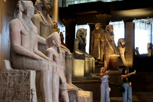 سياح يقفون بجوار المعروضات المتحفية المعروضة في المتحف المصري الكبير (رويترز)