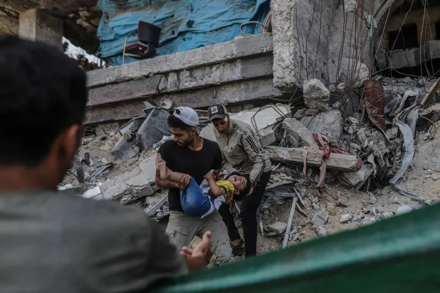 فلسطينيان يحملان طفلاً مصاباً إثر غارة إسرائيلية على حي الرمال بمدينة غزة أمس (إ.ب.أ)