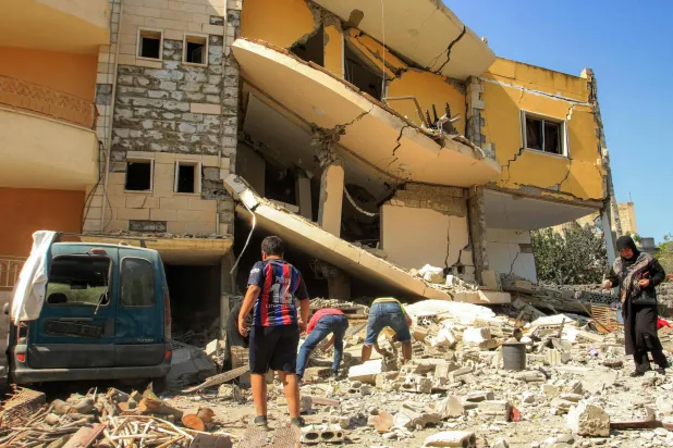 سكان يعاينون الدمار اللاحق بأحد الأبنية بعد استهداف إسرائيلي لبلدة عين قانا بجنوب لبنان ليل الخميس - الجمعة (أ.ف.ب)