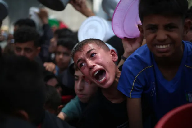 أطفال فلسطينيون بانتظار الطعام عند نقطة توزيع في النصيرات وسط قطاع غزة (أ.ف.ب)