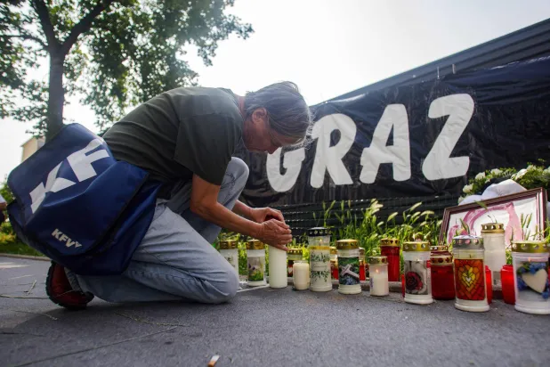 امرأة تُشعل شمعة عند نصب تذكاري مؤقت أمام المدرسة في غراتس بجنوب شرقي النمسا اليوم (أ.ف.ب)