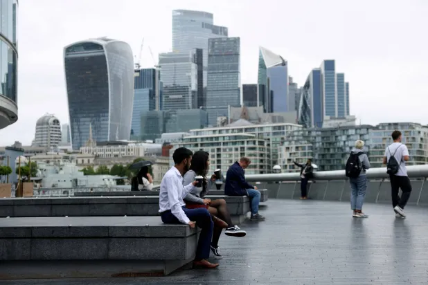 أشخاص يشربون القهوة الجاهزة في مواجهة أفق حي المال في لندن (رويترز)