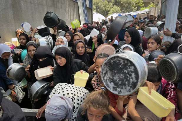 نازحون فلسطينيون يتجمعون في مطبخ خيري لتلقي وجبات الطعام في ظل نقص الغذاء بالنصيرات (د.ب.أ)