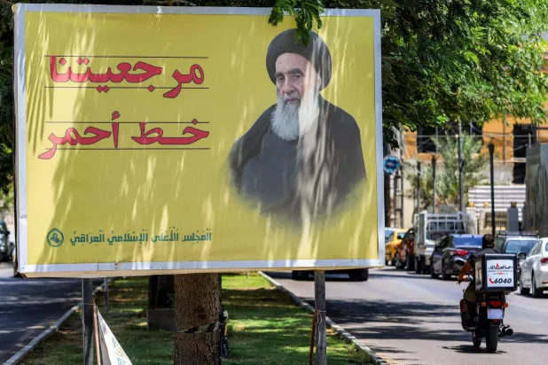 A man rides a motorcycle past a billboard depicting Iraq's top Shiite cleric, Ali al-Sistani, along a street in Baghdad on June 19, 2025. (Photo by AHMAD AL-RUBAYE / AFP)