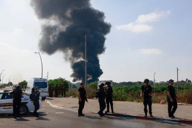 عناصر من الشرطة الإسرائيلية تقف بينما يتصاعد دخان جراء غارات إيرانية على موقع في هرتسليا قرب تل أبيب (أ.ف.ب)