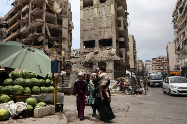 لبنانيات في الضاحية الجنوبية لبيروت على مقربة من مبان مدمرة ومتضررة نتيجة القصف الإسرائيلي (رويترز)