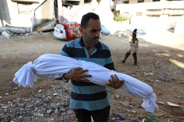 رجل يحمل جثمان طفل قتل خلال قصف إسرائيلي في مستشفى الشفاء في مدينة غزة (رويترز)