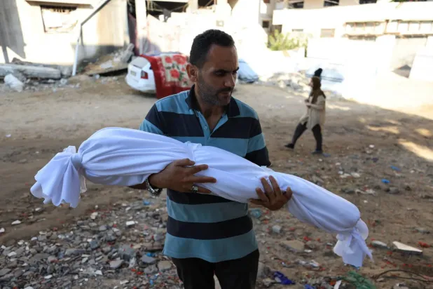 Gazze'deki Şifa Hastanesi'ne düzenlenen İsrail hava saldırısında öldürülen bir çocuğun cenazesini taşıyan bir adam (Reuters)