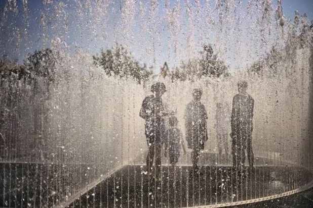 أشخاص يحاولون تبريد أنفسهم داخل نافورة في بون بألمانيا وسط ارتفاع درجات الحرارة (أ.ب)