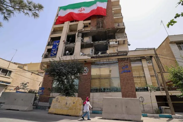 A woman walks past a residential building that was hit in an Israeli strike covered with a big Iranian flag, in Tehran on June 25, 2025. (AFP)