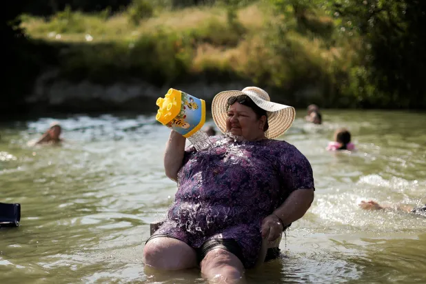 سيدة تجلس وسط مياه نهر إيرينيك في كوسوفو وتصب المياه على جسدها لتبريده وسط موجة حر (رويترز)