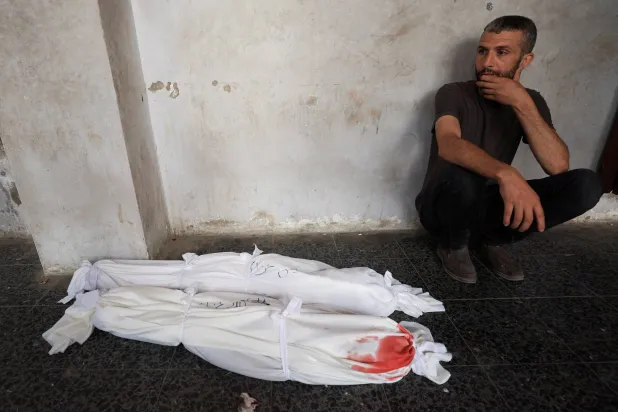 فلسطيني يجلس قرب جثث أطفال قُتلوا بغارة إسرائيلية على منزل قبل تشييعهم من مستشفى في مدينة غزة يوم الأحد (رويترز)