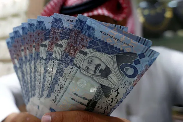 صراف سعودي يعرض أوراقاً نقدية بالريال السعودي في محل صرافة (رويترز)