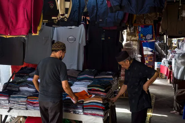 A vendor (L) assists a customer at a roadside clothing stall in Jakarta on June 30, 2025. (Photo by BAY ISMOYO / AFP)