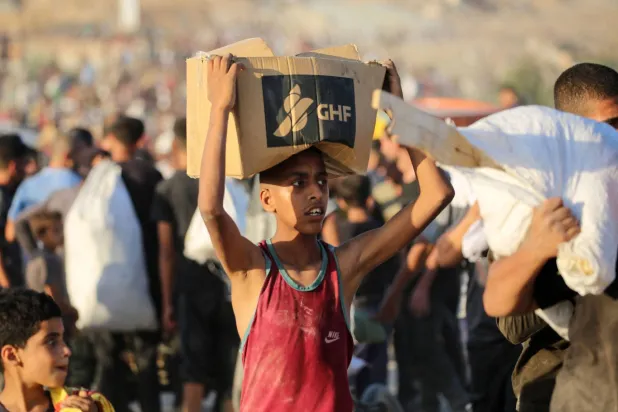 شاب يحمل طرد مساعدات من «مؤسسة غزة الإنسانية» يسير على طول طريق صلاح الدين بالقرب من مخيم النصيرات للاجئين في شمال قطاع غزة... 25 يونيو 2025 (أ.ف.ب)