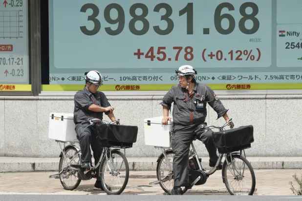 راكبو دراجات في أحد شوارع العاصمة اليابانية طوكيو يمرون أمام لوحة إلكترونية تعرض حركة الأسهم (أ.ب)