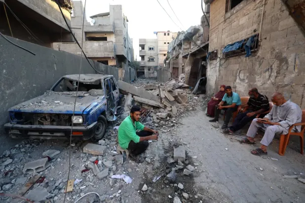 İsrail'in Gazze Şeridi'nin orta kesimindeki el-Bureyc Mülteci Kampı’na yönelik bombardımanında hasar gören bir arabanın yanında oturan Filistinliler (AFP)