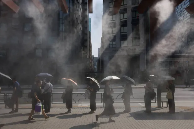 يابانيون ينتظرون حافلة في أحد شوارع العاصمة طوكيو في حين يتناثر فوقهم الرذاذ المرطب وسط موجة حر فائق (رويترز)