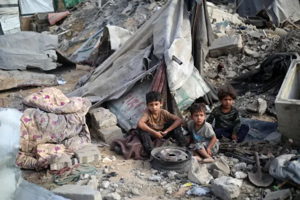 Filistinli çocuklar, İsrail'in dün Gazze Şeridi'nin merkezindeki el-Bureyc mülteci kampına düzenlediği hava saldırısının yol açtığı yıkımın ortasında (AFP)